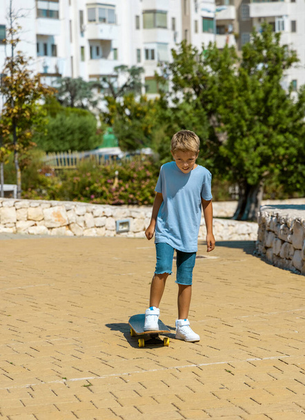 Preschooler kid boy in blue t-shirt learning to ride a skateboard outdoors. Cute child doing sports and having fun in park. Active hobbies, healthy lifestyle concept. T-shirt mockup - Photo, Image