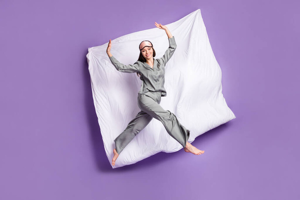 Full length body size photo of careless cheerful woman jumping on pajama party on bed isolated pastel purple color background - Foto, imagen