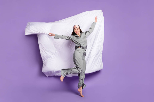 Full length body size photo of playful girlish woman jumping keeping pillow in grey sleepwear isolated pastel purple color background - Fotoğraf, Görsel