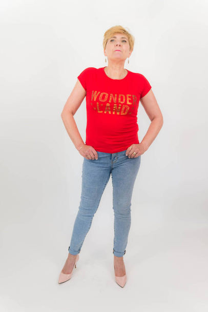 Mujer atractiva, bien formada y de mediana edad, con el pelo corto y rubio. Vestido con jeans, una camiseta roja. Sobre un fondo blanco. - Foto, imagen