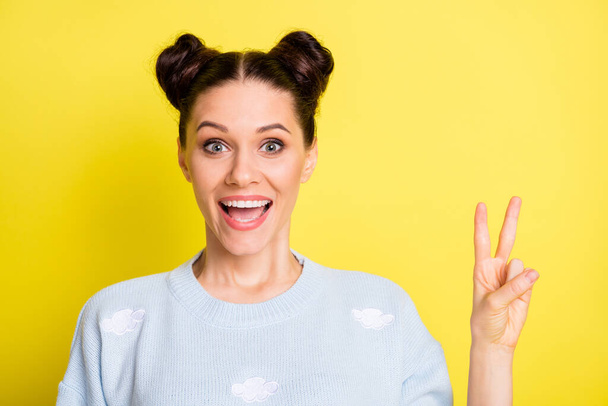 Photo of funny cheerful lady buns hairdo open mouth show v-sign wear blue pullover isolated yellow background - Foto, Bild