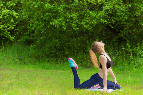 Beautiful young girl is engaged in sports, yoga, fitness on the beach by the river on a Sunny summer day - Photo, image
