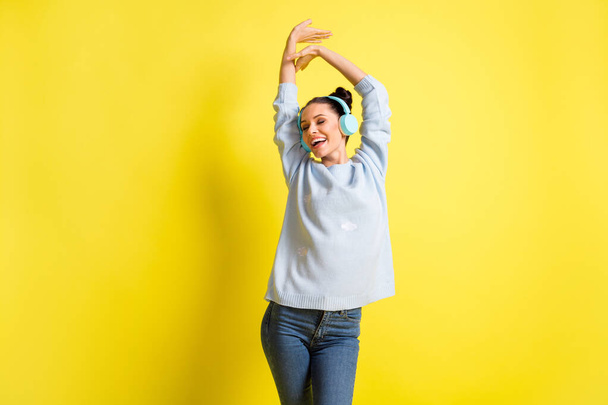 Photo of lady listen music dance close eyes raise arms wear headphones blue sweater jeans isolated yellow background - Fotó, kép