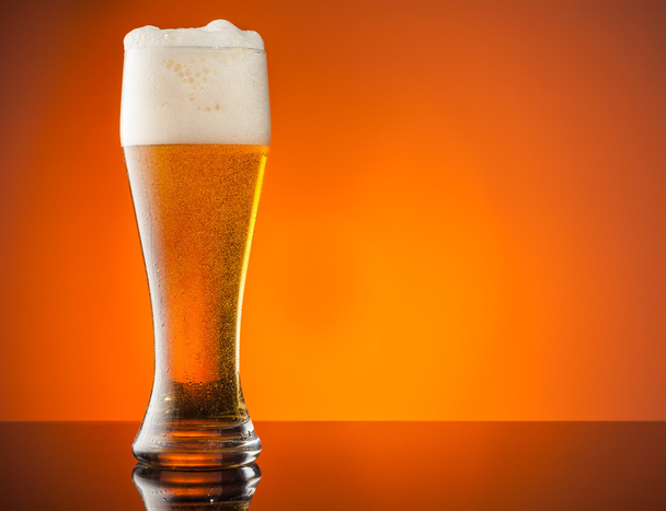 オレンジ色の背景とビールのグラス - 写真・画像