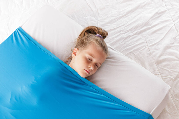 A cute blonde Caucasian girl sleeping on a mattress under a blue cozy blanket - Valokuva, kuva
