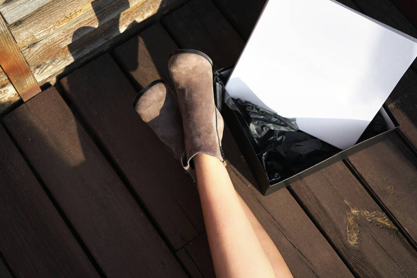 женские ноги в коричневых замшевых сапогах на деревянном фоне. женщина примеряет новые зимние туфли                   - Фото, изображение