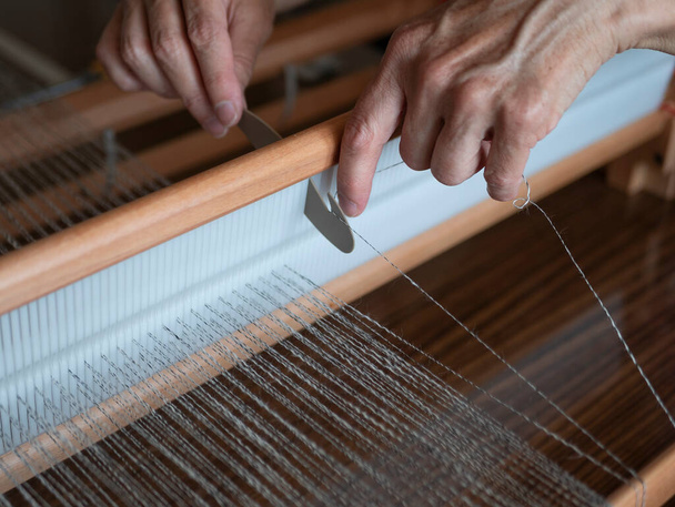 Woman is warping a wooden handloom. Hands holding a heddle hook and threading the table loom. Weaving tools - Foto, Bild