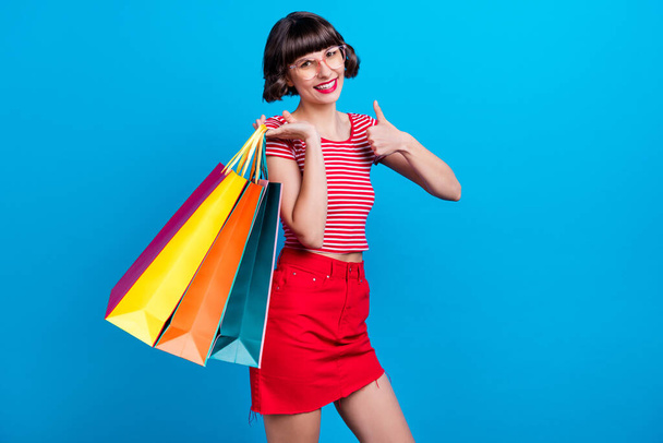 Photo portrait girl smiling keeping bags after shopping showing thumb-up isolated vibrant blue color background - Foto, immagini