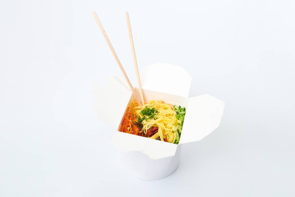 Rice wok with seafood and vegetables in white box and wooden chopsticks isolated on white background, close up. Open takeout box with wok and bamboo sticks. Asian food, fast food delivery concept - Photo, Image