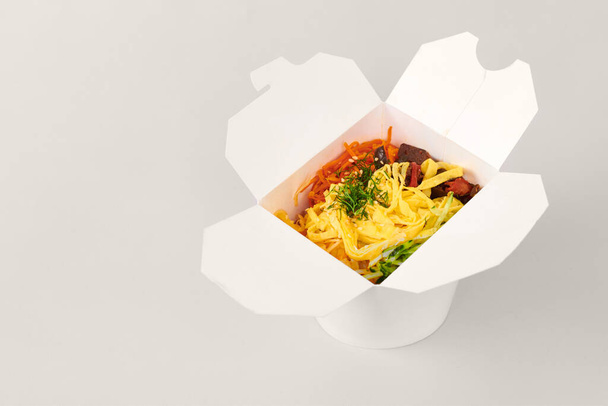 Arroz wok con mariscos y verduras en caja blanca aislado sobre fondo gris. Una caja abierta para llevar con wok de arroz, cóctel de mariscos y verduras. Comida para llevar, concepto de entrega de comida rápida - Foto, Imagen
