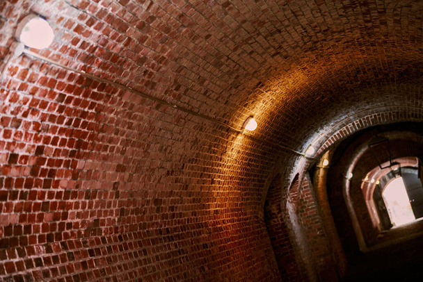 Cihlový tunel ve staré německé pevnosti, podkrovní chodba z červených cihel se starými dráty, průmyslový sklep tajné vojenské základny. Tajná chodba starého sídla. Fort No. 5 King Frederick William III - Fotografie, Obrázek