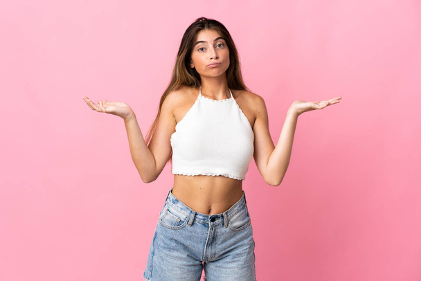 Young caucasian woman isolated on pink background having doubts while raising hands - Photo, Image