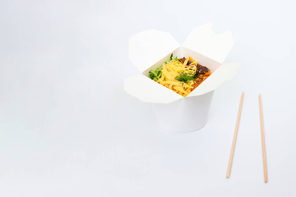 Reiswok mit Meeresfrüchten und Gemüse in weißer Schachtel und Holzstäbchen isoliert auf weißem Hintergrund, Kopierraum. Offene Take-out-Box mit Wok und Bambusstäben. Asiatisches Essen, Fast Food Lieferkonzept - Foto, Bild