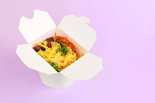 Wok ryżowy z owocami morza i warzywami w białym pudełku izolowanym na fioletowym tle. Jedno otwarte pudełko na wynos z wokiem ryżowym, koktajlem z owoców morza i warzywami. Jedzenie na wynos, koncepcja fast food - Zdjęcie, obraz