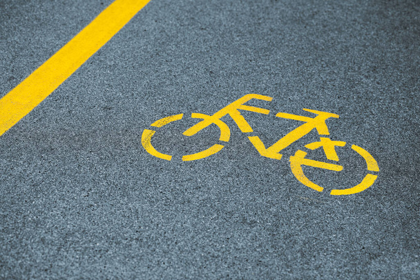 Yellow bicycle sign on cycling path, safe road traffic near highway. Painted bicycle road sign on asphalt bike lane, yellow marking for road traffic safety - Foto, immagini