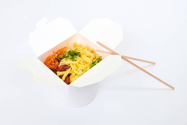 Rice wok with seafood cocktail and vegetables in box and wooden chopsticks isolated on white background, studio. Open takeout box with wok and bamboo sticks. Takeout and takeaway fast food concept - Photo, Image
