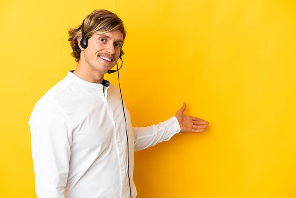 Человек-телемаркетолог, работающий с гарнитурой, изолированной на желтом фоне, разводящей руки в сторону для приглашения прийти - Фото, изображение