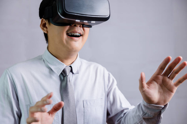 Un professeur thaï masculin portant des lunettes de réalité virtuelle avec un geste amusant et passionnant touche un modèle sur un fond blanc avec sa main. - Photo, image