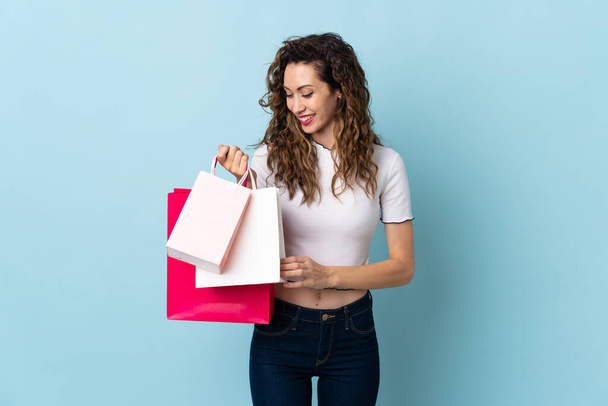 Young caucasian woman isolated on blue background holding shopping bags - Photo, Image