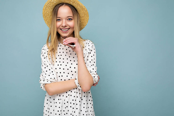 Young beautiful woman. Trendy woman in casual summer dress and straw hat. Positive female shows facial emotions. Funny model isolated on blue background with free space - Fotografie, Obrázek