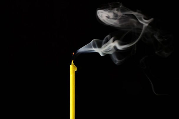 extinguished candle with a smoldering wick exudes smoke on a black background. High quality photo - Fotografie, Obrázek