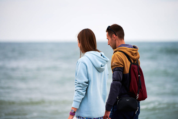 Baltiysk, Oroszország - 08.01.2021 - Szerető pár, akik cipőben a kezükben sétálnak a tengerparton. Fiatal férfi és nő randizik a Balti-tengeren. Őszinte pár beszél a romantikus kapcsolatukról. - Fotó, kép