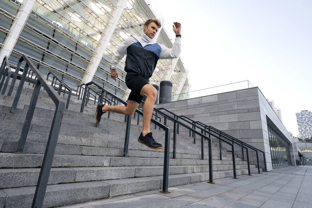 Δυναμική κίνηση. Χαμηλή γωνία άποψη του νεαρού αθλητή άλμα από τα σκαλιά, ενώ τρέχει και την κατάρτιση σε εξωτερικούς χώρους στην πόλη. Ο αθλητισμός είναι ο τρόπος ζωής. Έννοια διαφήμισης - Φωτογραφία, εικόνα