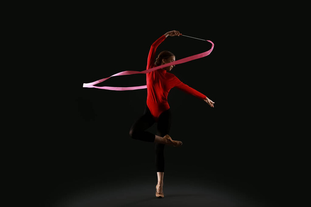 Piękna młoda kobieta robi gimnastykę ze wstążką na czarnym tle - Zdjęcie, obraz