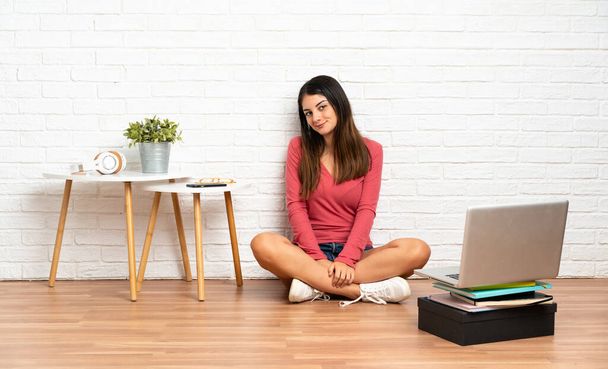 Молодая женщина с ноутбуком сидит на полу в помещении. Портрет - Фото, изображение