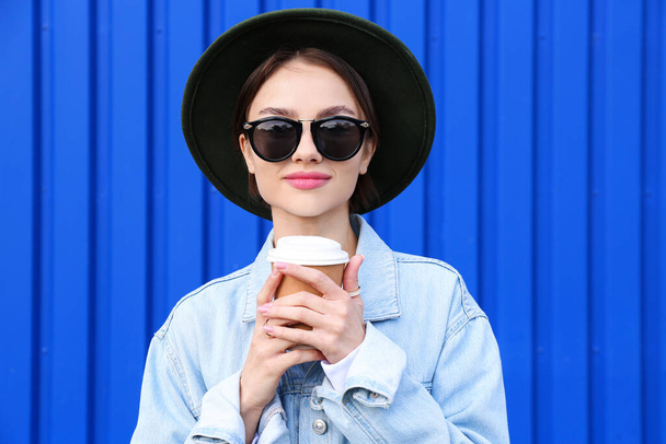 Portrait of young fashionable woman with paper cup of tea on blue background - Photo, Image