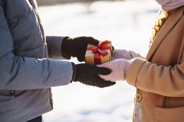 Exchange of Christmas gifts. Young couple exchange bright box with gift  in the snowy forest. Nature, holidays, rest, travel concept - Φωτογραφία, εικόνα