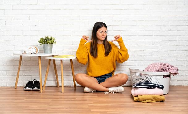 Young woman sitting on the floor at indoors with clothes basket proud and self-satisfied - Photo, Image