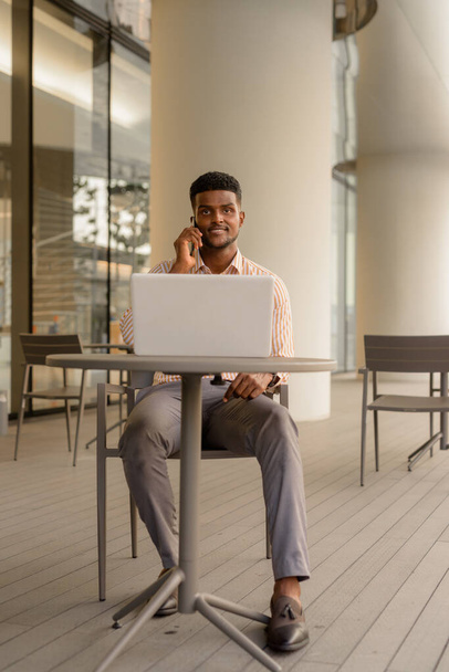 Портрет молодого привлекательного африканского бизнесмена с ноутбуком в кофейне - Фото, изображение
