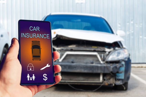壊れた車の後にオンラインで自動車保険のアプリケーションを使用するためにスマートフォンを保持ハンサムな男の手。保険の概念. - 写真・画像
