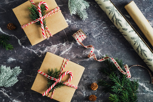 Christmas holiday preparation concept. Craft paper gift boxes decorated striped ribbon, fir branch and candy cane on slate table. - Foto, Imagem