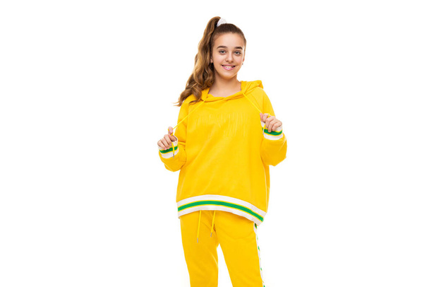 Beautiful funny happy wonderful smiling cute girl with dark hair with ponytail in stylish yellow tracksuit with green stripes isolated on white background with empty space for text - Foto, imagen