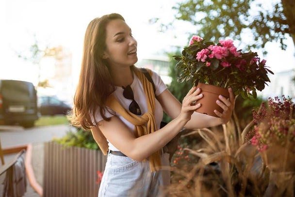 Photo of european beautiful attractive positive happy brunette woman wearing stylish white t-shirt and blue jeans chooses flowers as a gift in a street garden stall in the town - Foto, imagen