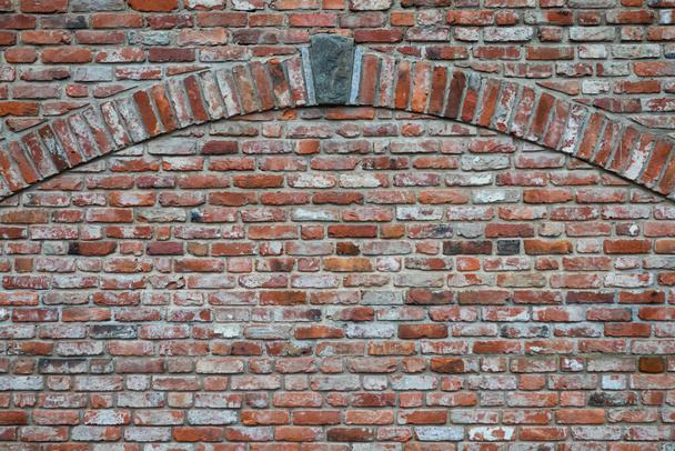 Старая красная кирпичная стена. Существует декоративный элемент в виде арки с краеугольным камнем. Фон. Текстура.  - Фото, изображение