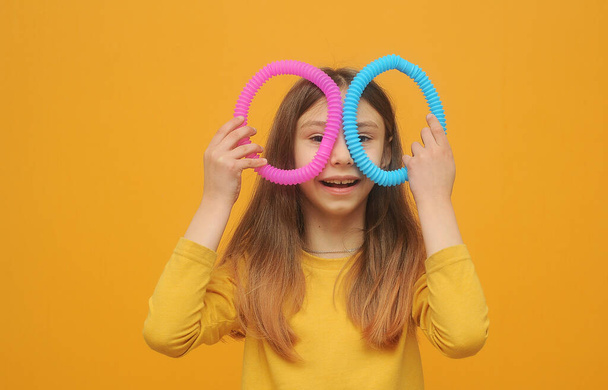 pequeña chica inteligente en ropa amarilla juega con el tubo pop de juguete de moda - Foto, Imagen