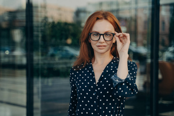 Beautiful redhead woman poses near office building against blurred background - Фото, изображение