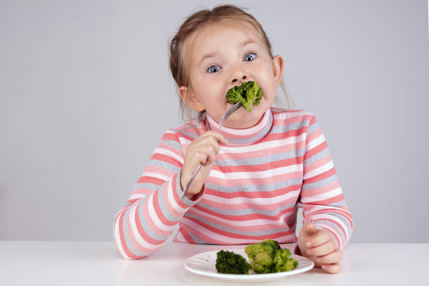 The child eats broccoli with an appetite. Organic Cabbage and food on a plate. Green healthy vegetables rich in vitamins. - Foto, afbeelding