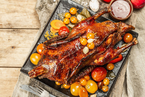 Whole roast duck stuffed with apples. Poultry served with pickled vegetables. A festive dish for Christmas, Thanksgiving Day, or any holiday. Wooden background, cutlery, top view - Fotó, kép