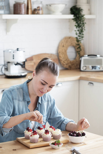 Cooking, Home Business, Freelance, People and Hobbies concept: Young woman pastry chef decorates cupcakes with berries - Photo, Image