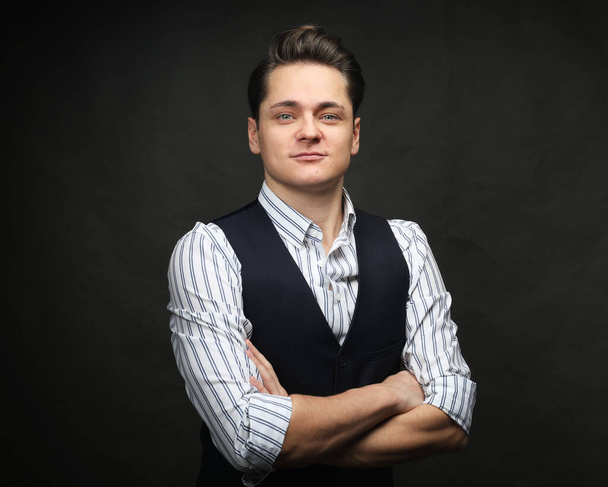 Young fashionable handsome man wearing elegant shirt and vest over black background smiling with crossed arms looking at the camera. - Fotografie, Obrázek