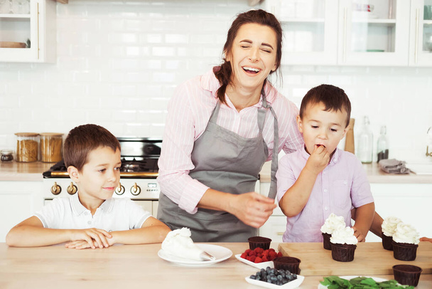 Happy family in the kitchen. Mom and two little boys, brothers make homemade cupcakes. - Photo, Image