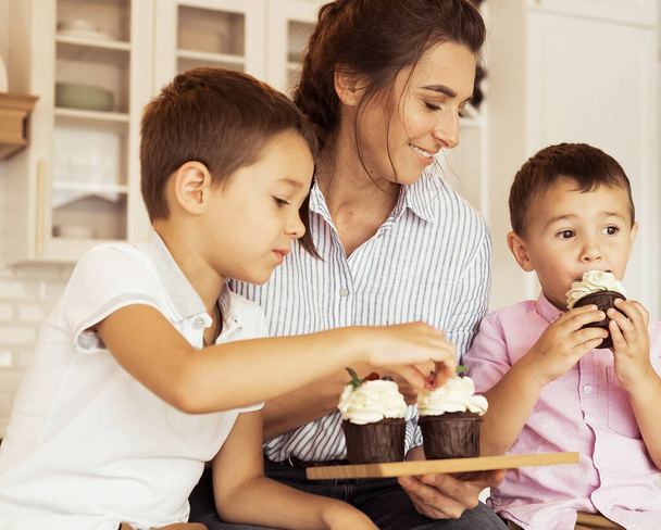 Happy family in the kitchen. Mom and two little boys, brothers, are eating homemade cupcakes. - Foto, Imagem