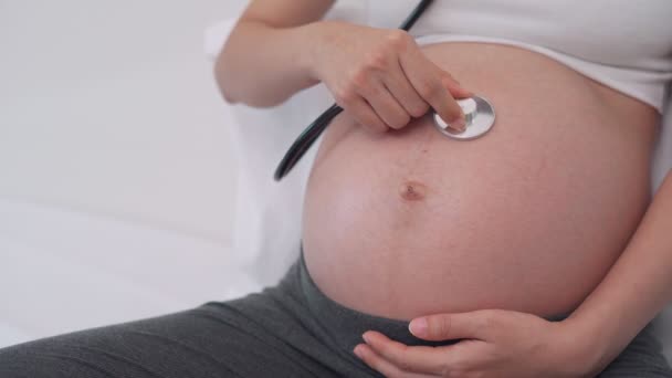 A terhes nő sztetoszkóppal hallja a baba hangját. Hallgatni a meg nem született gyermek hangját, aki lehetséges rendellenességeket észlel a meg nem született gyermekben. A terhes nők boldogságának fogalma. - Felvétel, videó