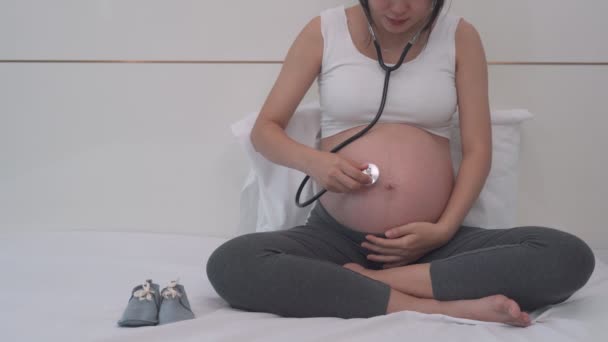 έγκυος γυναίκα χρησιμοποιεί στηθοσκόπιο για να ακούσει την καρδιά του μωρού. Ακούγοντας τις φωνές του αγέννητου παιδιού δημιουργείται μια σχέση μεταξύ της μητέρας και του αγέννητου παιδιού. έννοια ευτυχία της εγκυμοσύνης. - Πλάνα, βίντεο