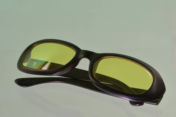Reflectie van een zonnebril. Groene zonnebril, close-up. Een zonnebril. Oude stijl zonnebril. Bril met transparante lenzen. Vintage zonnebril op gereflecteerde achtergrond. Sluiten van versleten zonnebril - Foto, afbeelding