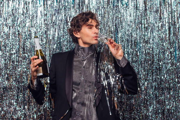 Holidays concept - happy tipsy man with bottle of champagne and wine glass at christmas or new year party on a sparkle background. - Fotografie, Obrázek